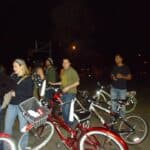 Group of people standing with bicycles at night, likely chatting near a bike ride meetup.