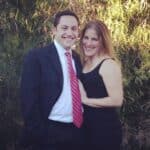Smiling couple posing in formal attire outdoors with greenery in the background.