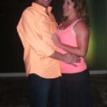 Smiling man in a peach shirt dancing with a woman in a pink tank top outdoors at night.