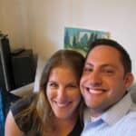 Couple smiling for a selfie on a couch in a living room with a painting in the background.